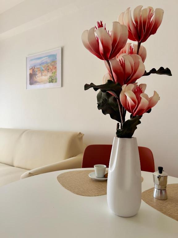 a white vase with pink flowers on a table at DaMa s Apartment on the beach in Giardini Naxos