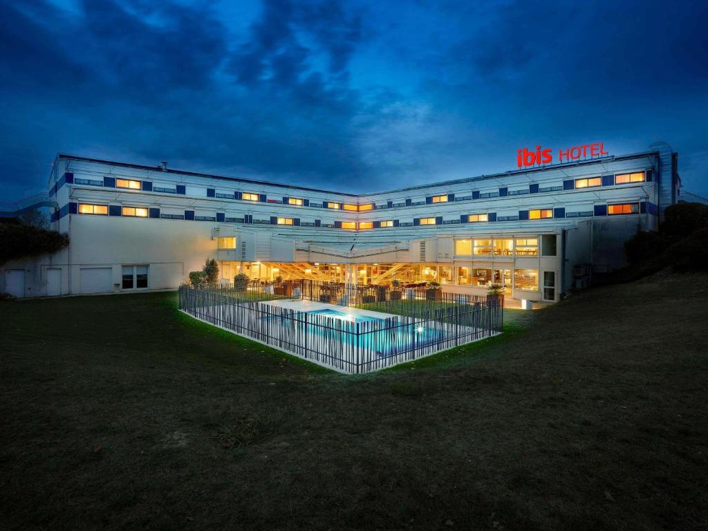 a building with a pool in front of it at night at ibis Poitiers Site du Futuroscope in Chasseneuil-du-Poitou