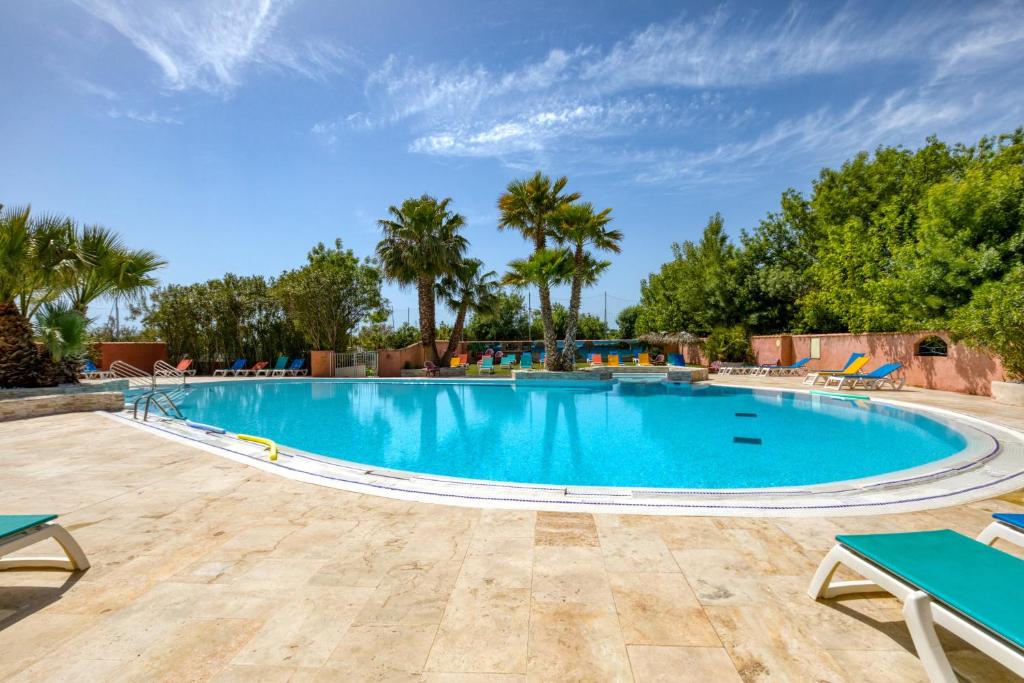a large swimming pool with palm trees in the background at Bungalow in Agde