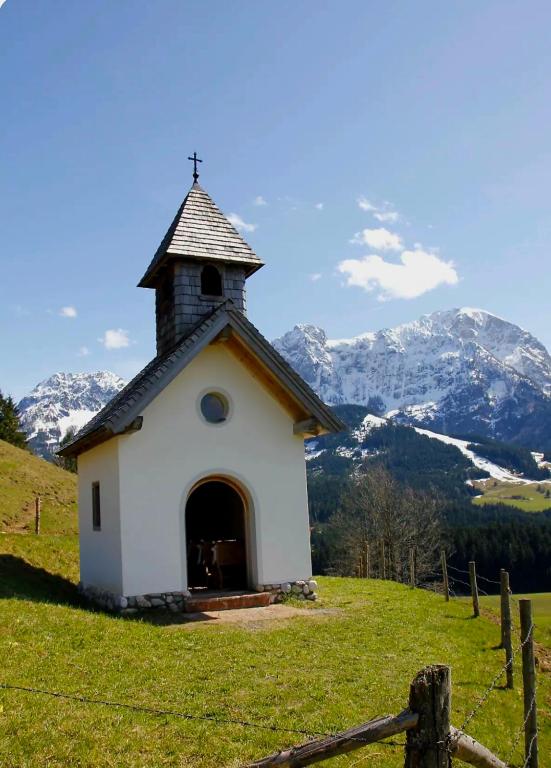 a small chapel on a hill with mountains in the background at BUAMA Kammer in Abtenau