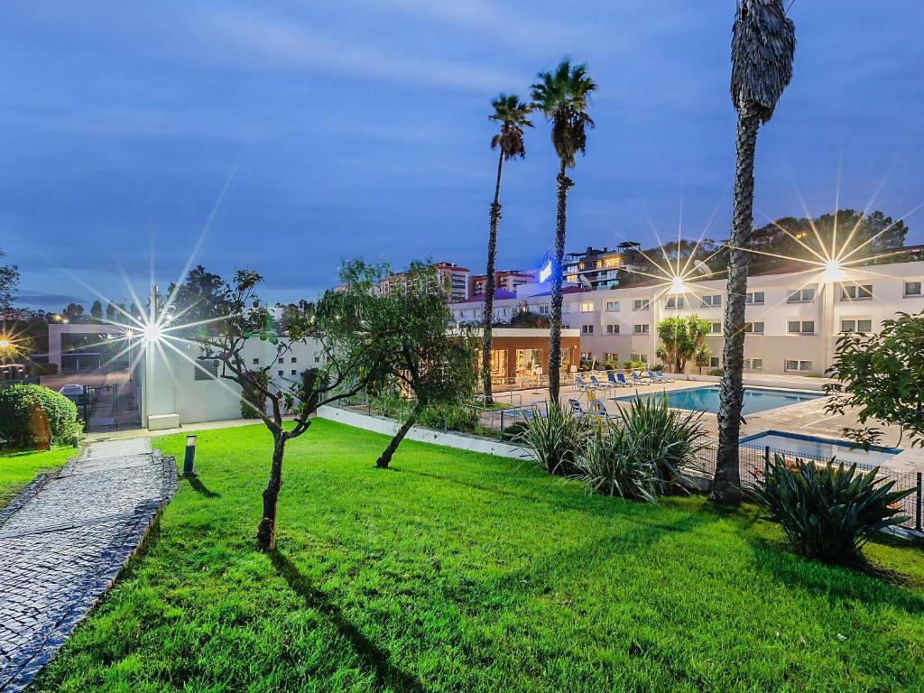 a park with palm trees and a pool at night at Novotel Setubal in Setúbal