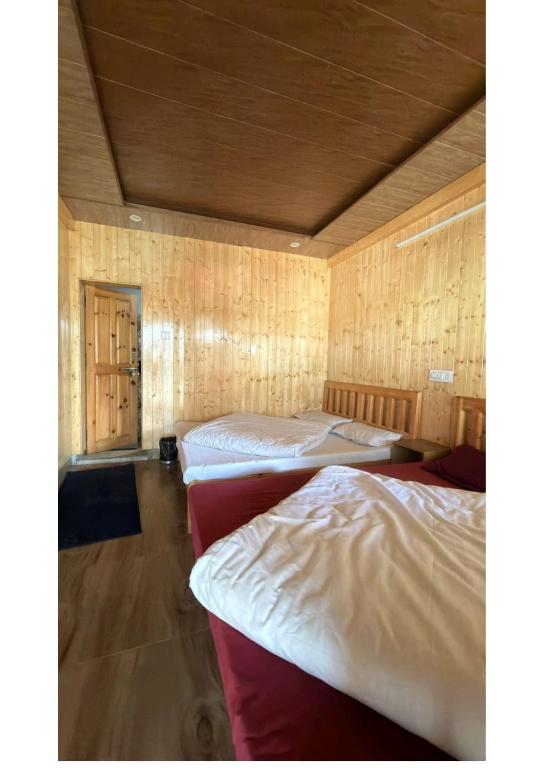 a room with three beds in it with wooden walls at Ekdantam Hotel and Restaurant in Uttarkāshi