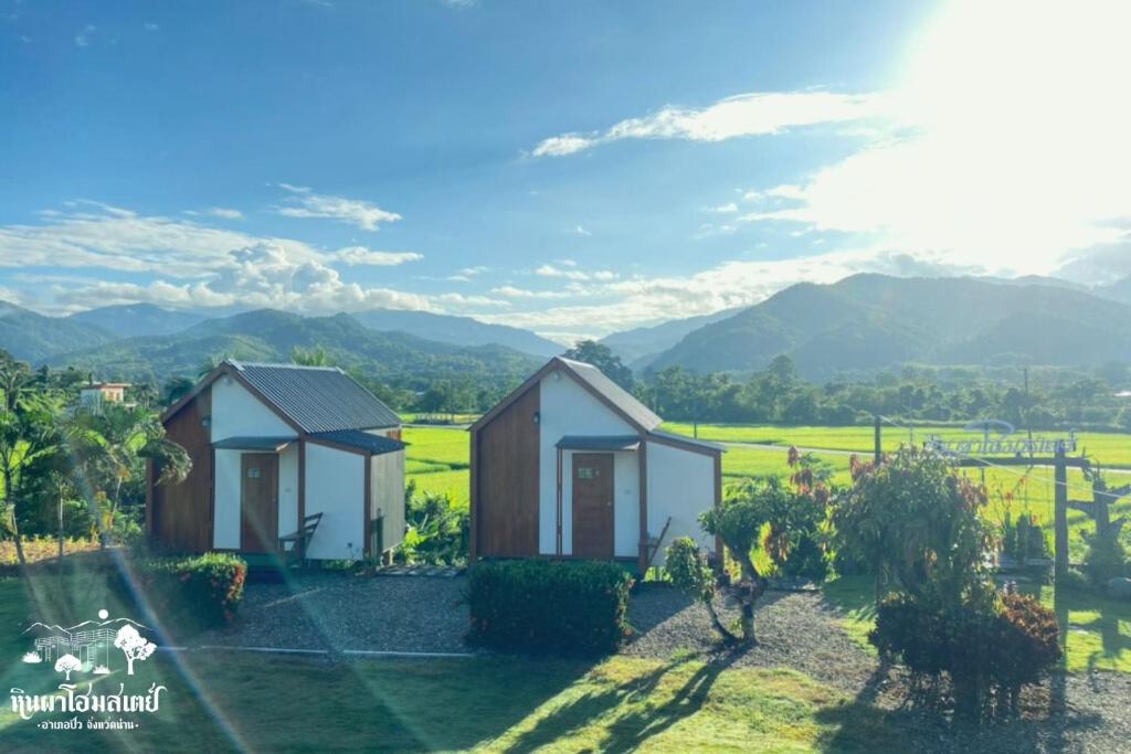 two houses in a field with mountains in the background at หินผาปัว รีทรีต & หินผาโฮมสเตย์ in Ban Choko