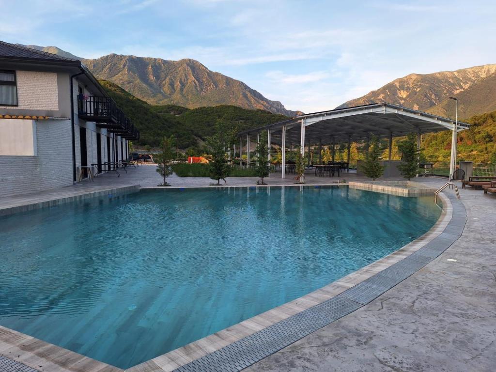 a swimming pool in front of a building with mountains at Lumi i Bardhe Hotel & Restaurant in Kuç