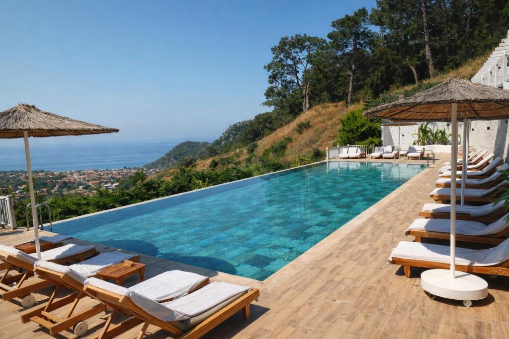 a pool with chairs and umbrellas and the ocean at Ölüdeniz Manzara Non Alcoholic Family Hotel in Oludeniz