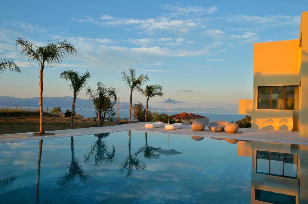 a swimming pool with palm trees and a building at Althea Resort in Áno Loutrón