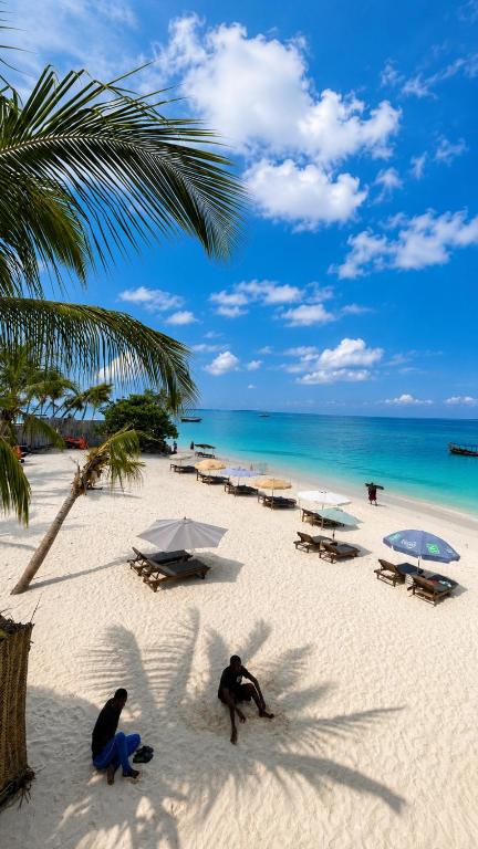 two people on a beach with umbrellas and the ocean at Zava Nungwi in Nungwi