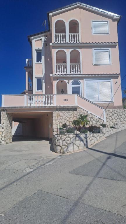 a large pink house with a balcony on a street at Apartmani Azik in Lopar