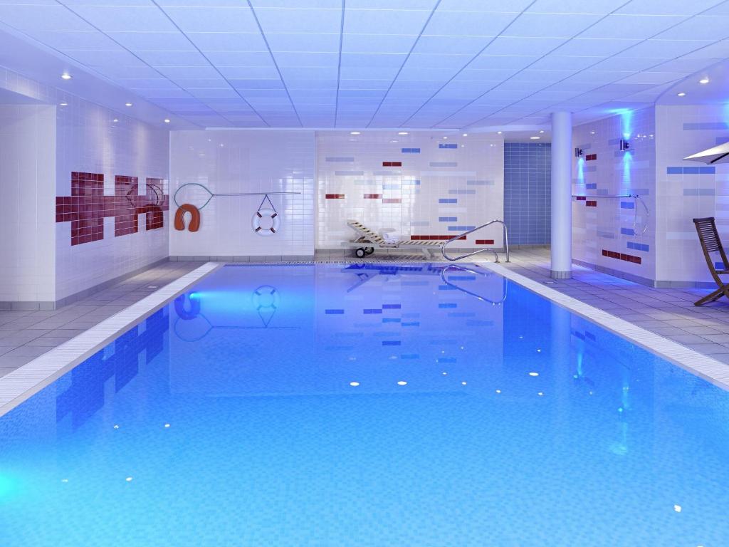 a large swimming pool with blue water in a room at Novotel Milton Keynes in Milton Keynes