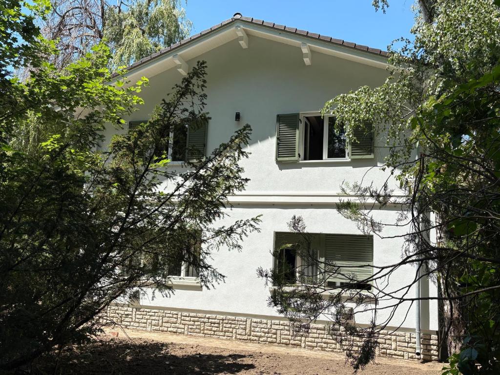 a white house with green shuttered windows and trees at Fűzfás Apartman in Siófok