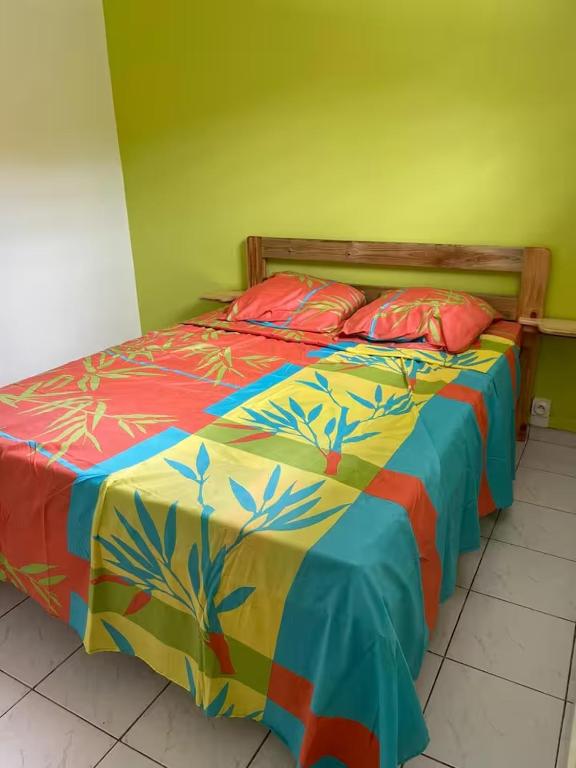 a bed with a colorful comforter and two pillows at Gites vallée des caraibes in Bouillante