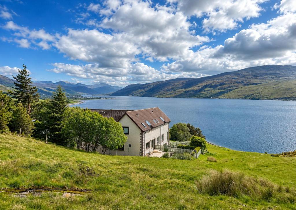 a house on a hill next to a body of water at Ardvreck House in Ullapool