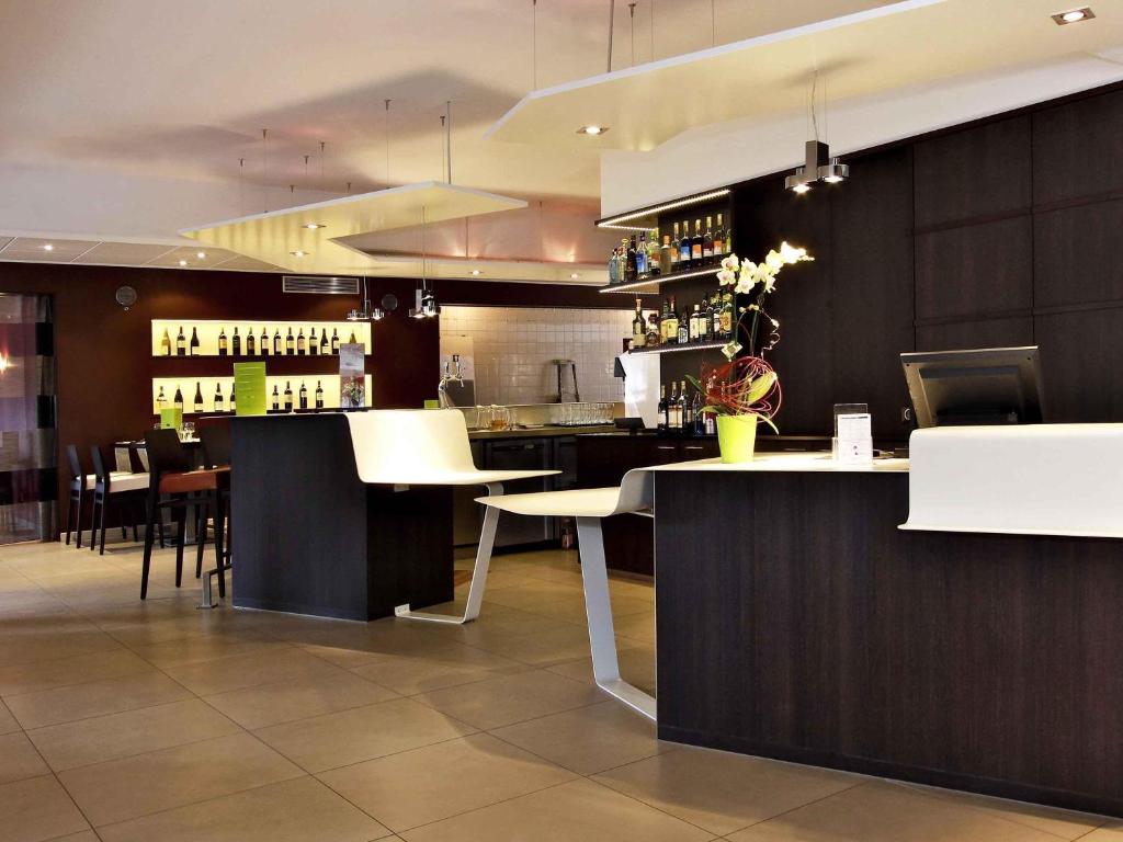a restaurant with a bar with white tables and chairs at Mercure Hexagone Luxeuil in Luxeuil-les-Bains