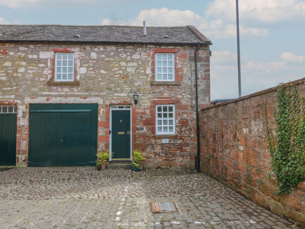 an old brick house with green doors and a brick wall at The Old Coach House in Lockerbie