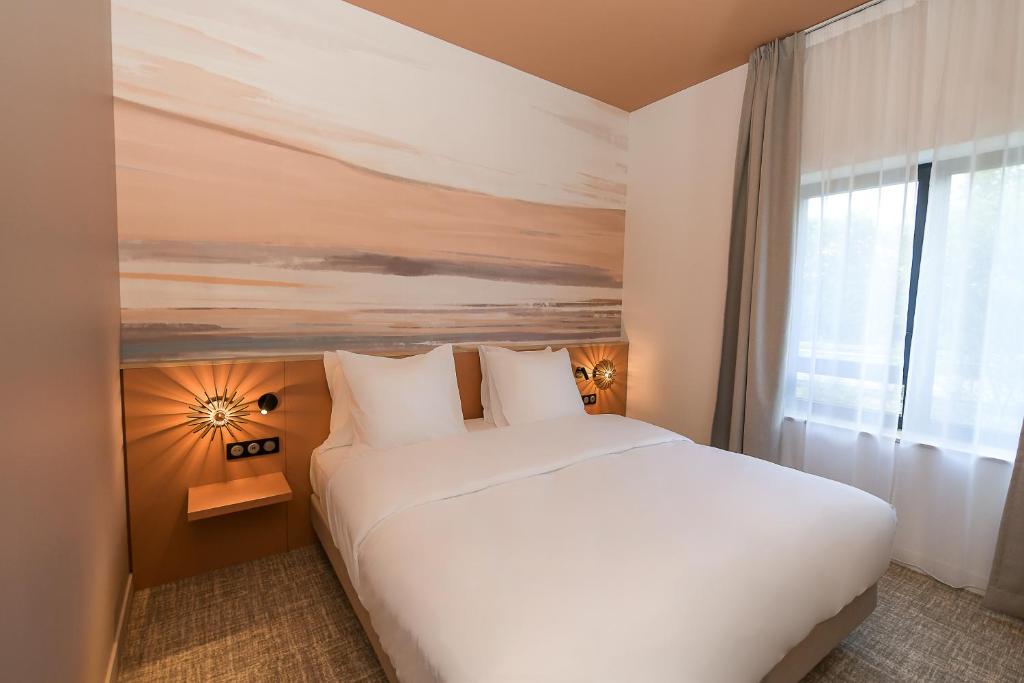 a bedroom with a large white bed and a window at The Originals Boutique, Osmo Hôtel, Rennes Sud Chantepie in Chantepie