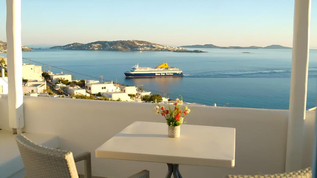 a balcony with a table and a cruise ship in the water at Aegean View Suites Mykonos in Agios Stefanos
