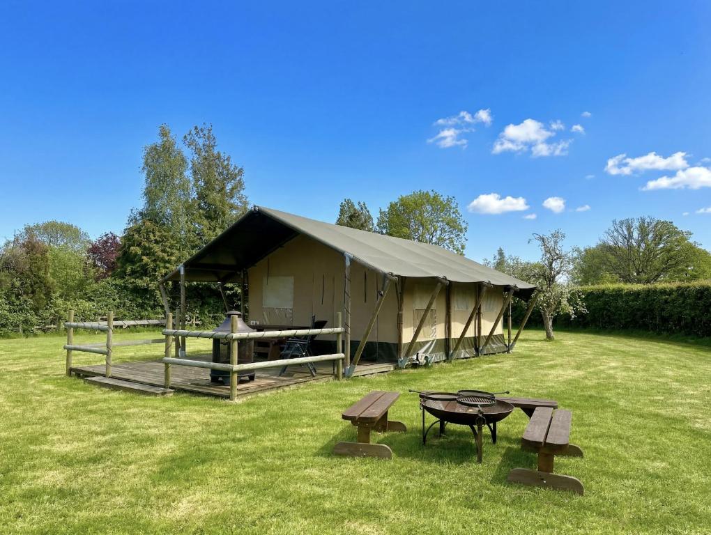 a tent in a field with a table and benches at The Firs Glamping in Welland
