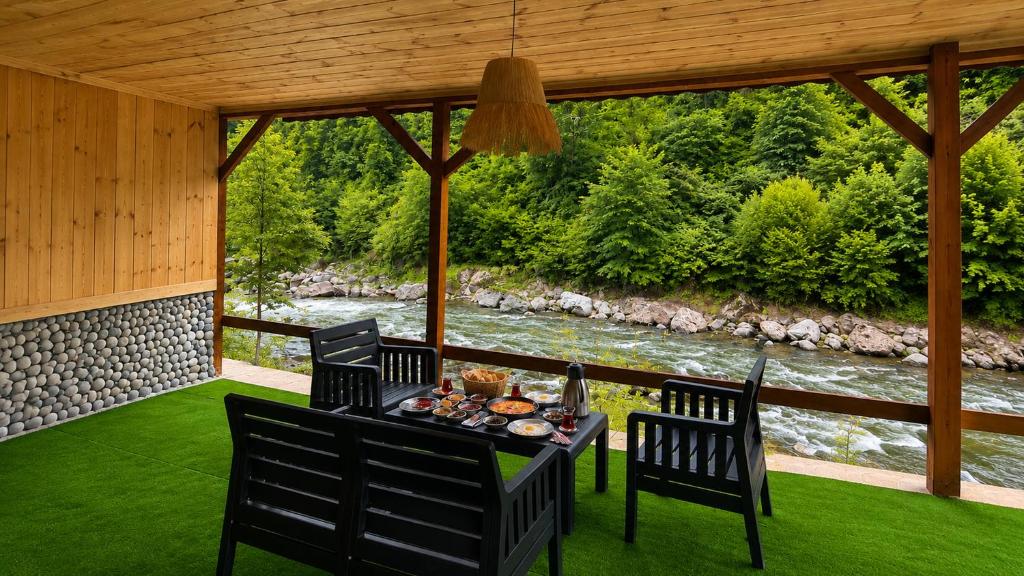 a table and chairs on a porch with a river at Ayder River Suite by Karadeniz in Ardeşen