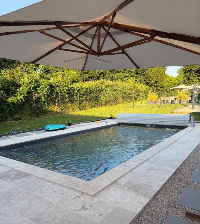 a swimming pool with an umbrella in a yard at Chalet en bois indépendant, terrasse et accès piscine in Montret