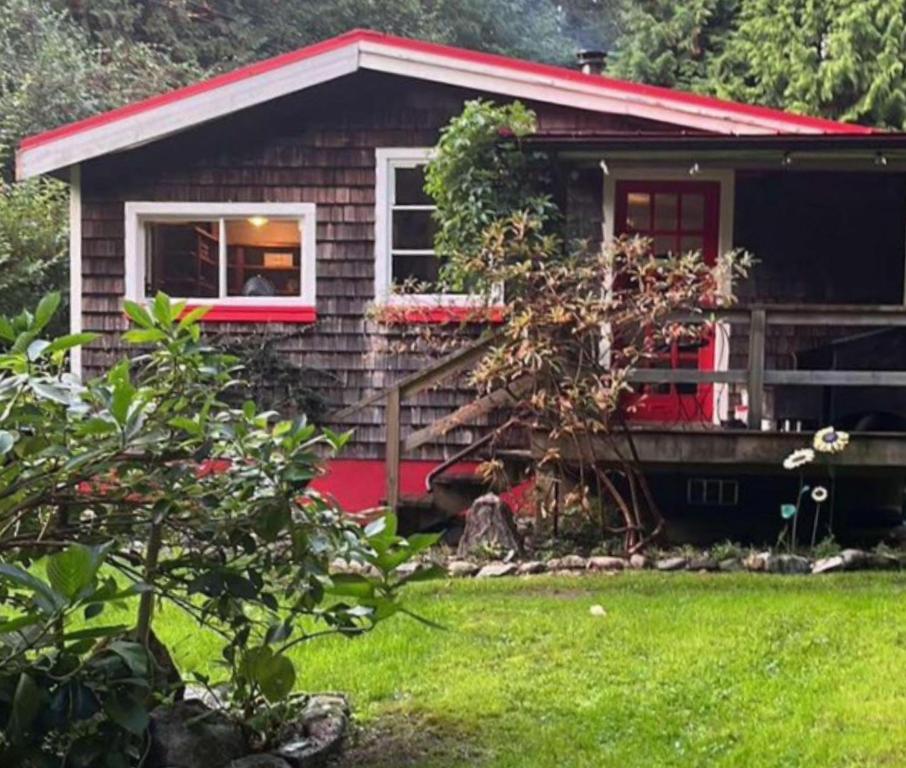 a small house with a red door and a yard at Cabin by the Creek in Roberts Creek