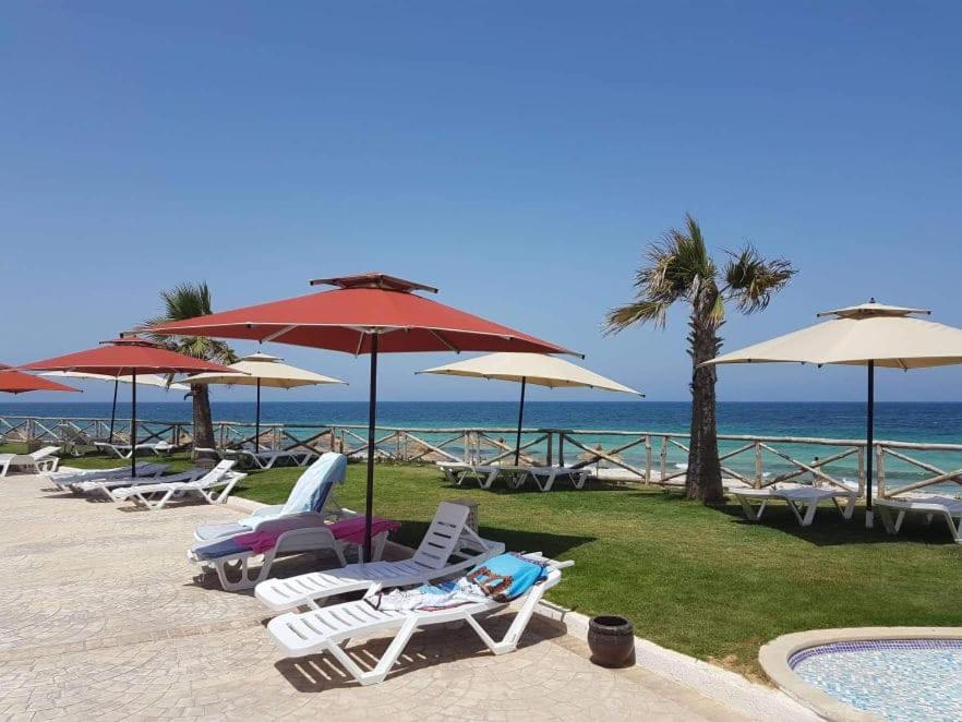 a group of lawn chairs and umbrellas next to the ocean at Studio S0 FOLLA RESORT CHATT MERIEM in Sousse