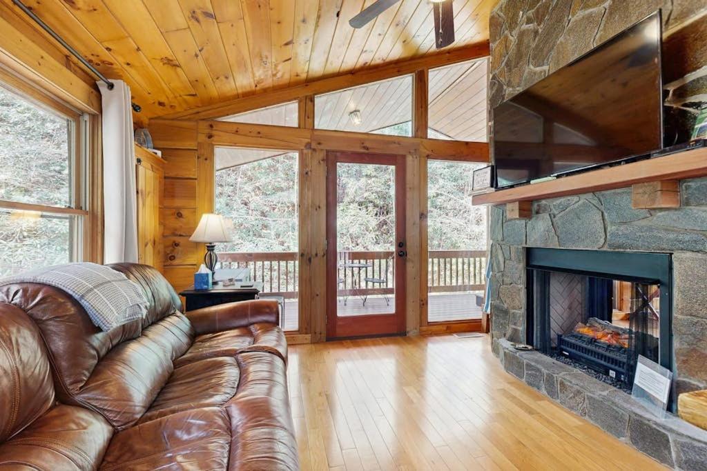 a living room with a leather couch and a fireplace at Creeksong Cabin in Topton