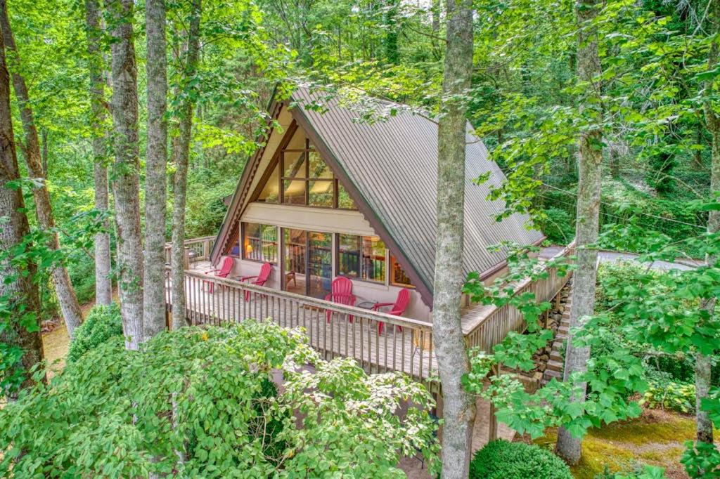 a cabin in the woods with red chairs and trees at Chalet at Peek's Creek in Franklin