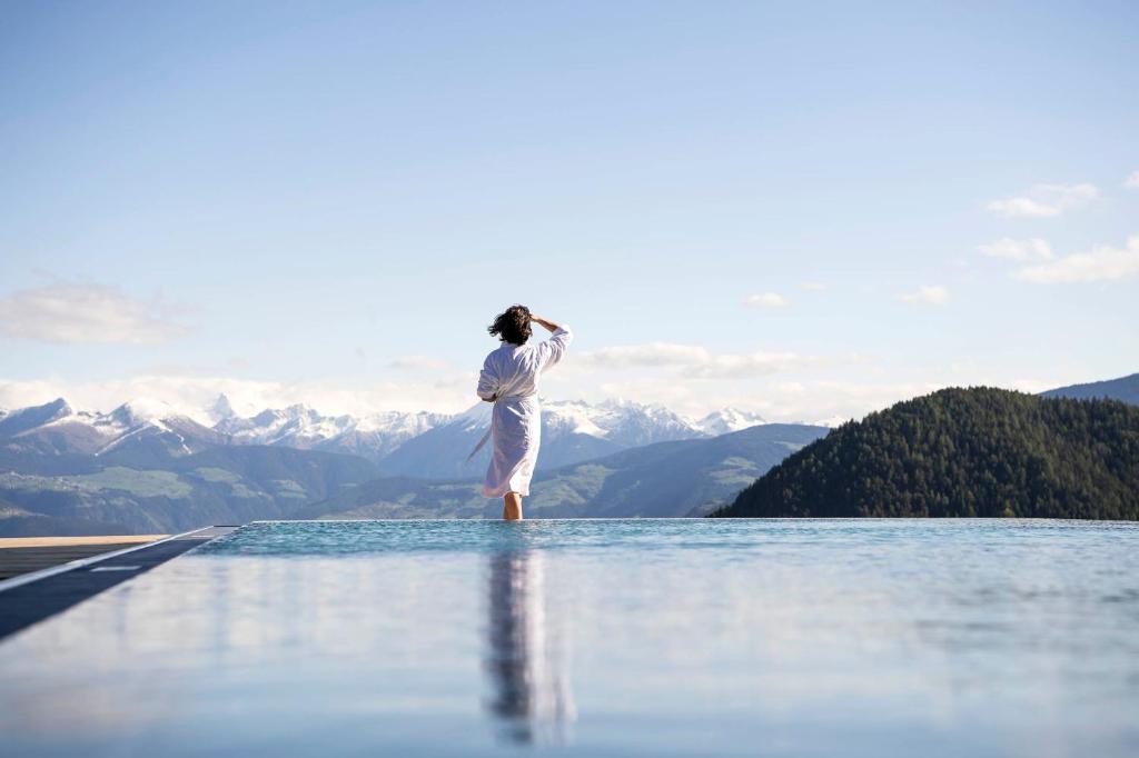 una donna in piedi sul bordo di una piscina con vista sulle montagne di Hotel Gnollhof a Chiusa