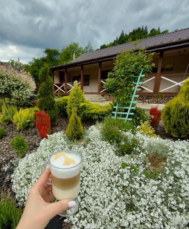 a person holding a cup of coffee in front of flowers at "Глиняна хатинка" in Beloberëzka