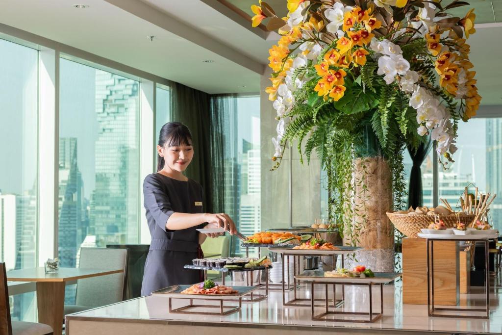 A staff member serves food at a bright buffet beside floor-to-ceiling windows.