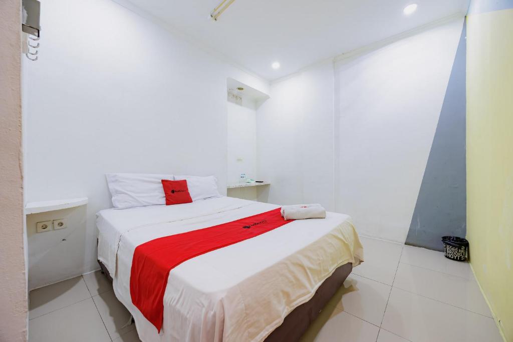 a white bedroom with a bed with a red blanket at RedDoorz at Taman Galaxy Bekasi in Bekasi