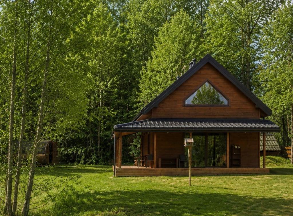 a small wooden cabin in a field with trees at Dom przy Lesie z sauną in Augustów