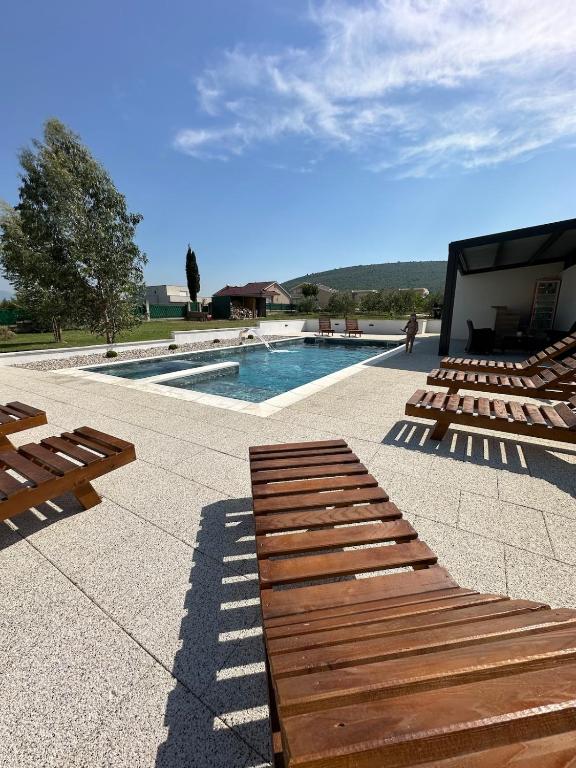 a swimming pool with wooden benches next to a building at Kuća za odmor Nina in Čapljina