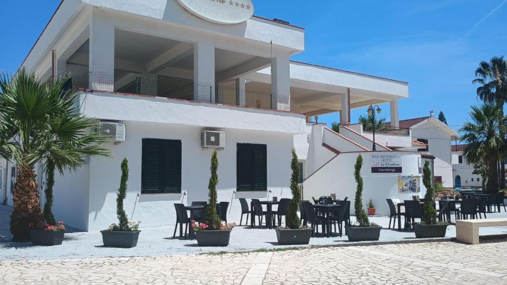 a white building with tables and chairs and palm trees at Hotel Tre Lanterne in Marina di Sibari