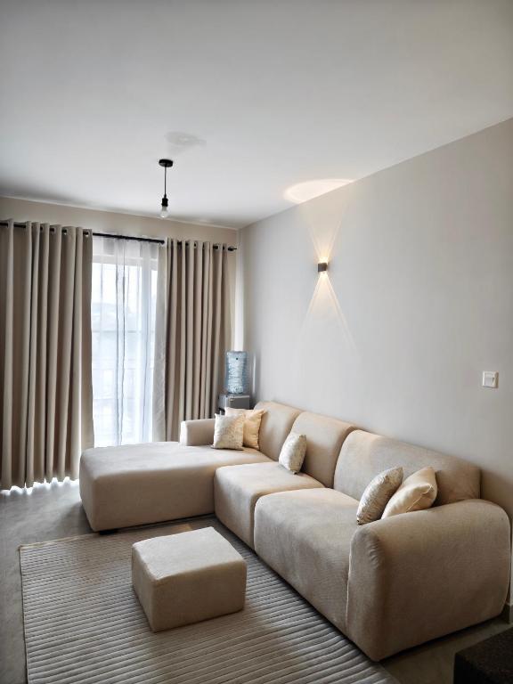 a living room with a large couch and a large window at Chic One Bedroom Apartment near The Kenya School of Government - KSG in Nairobi