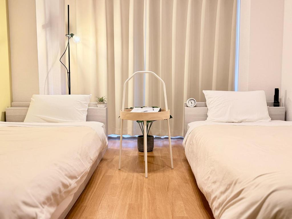 two beds with white sheets and a table between them at ura 東横のヨコ301 in Kaigandōri