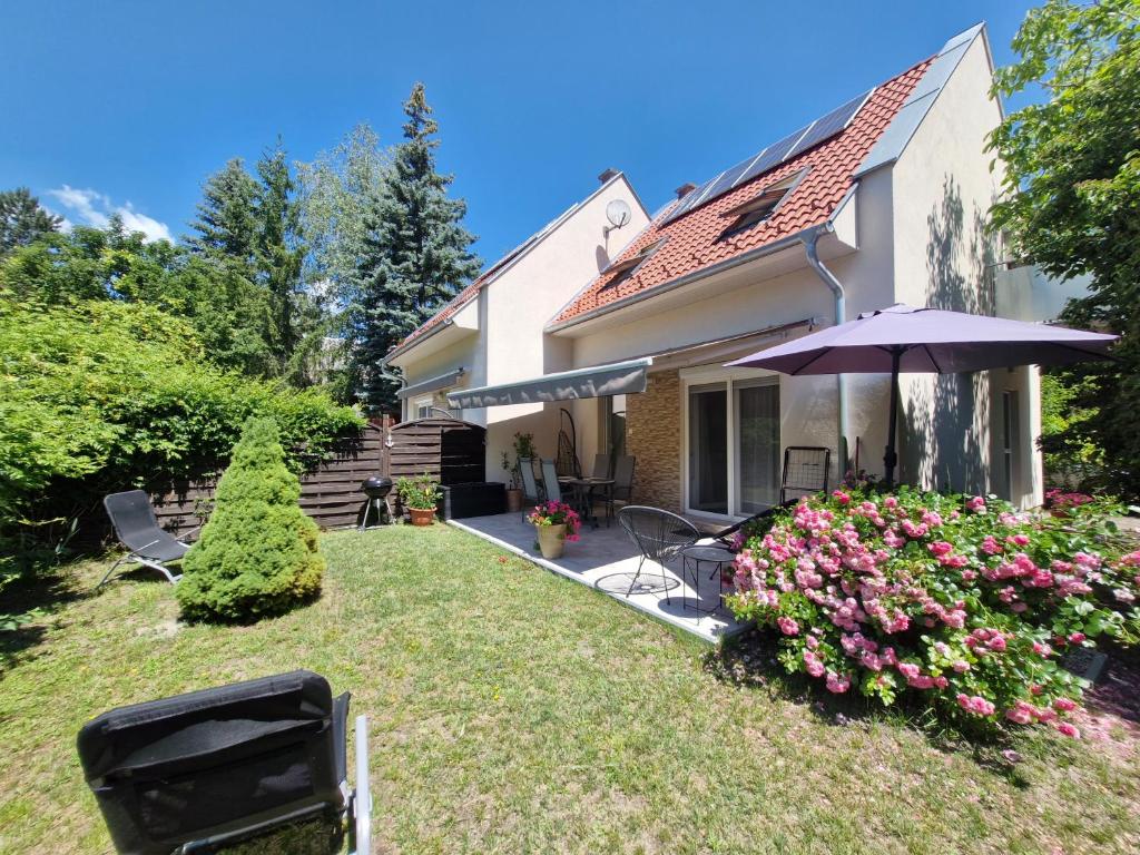 a yard with a house with an umbrella and flowers at Fenyves Ferienhaus 2 **** in Balatonfenyves