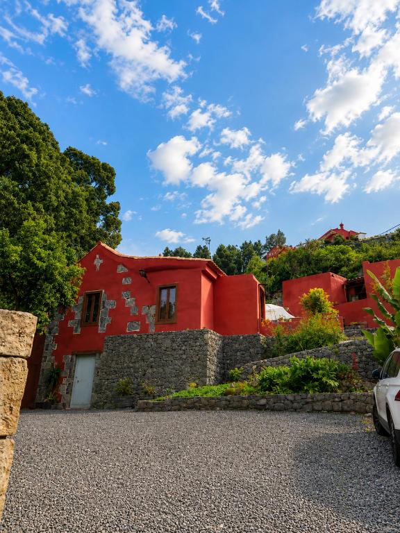 a red house with a stone wall and trees at Finca La Acequia del Gamonal in Santa Brígida