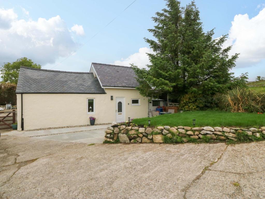 a white house with a stone wall and a tree at Ty Loti in Caernarfon