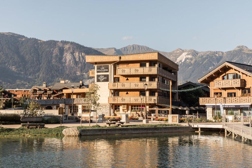 a building next to a body of water with mountains at Hôtel Les Peupliers in Courchevel