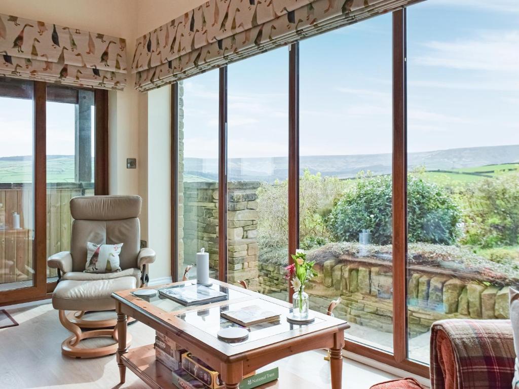 a living room with a table and a chair and large windows at Shelduck Cottage in Holmfirth