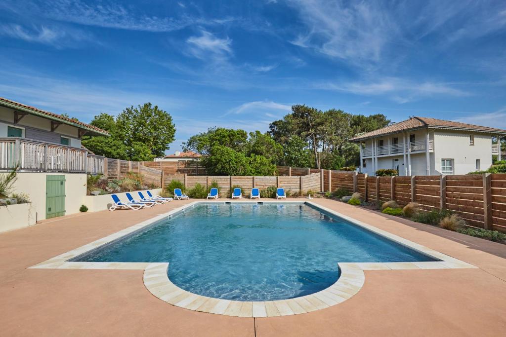 a swimming pool with chairs and a fence at Résidence Odalys Bleu Ocean in Moliets-et-Maa