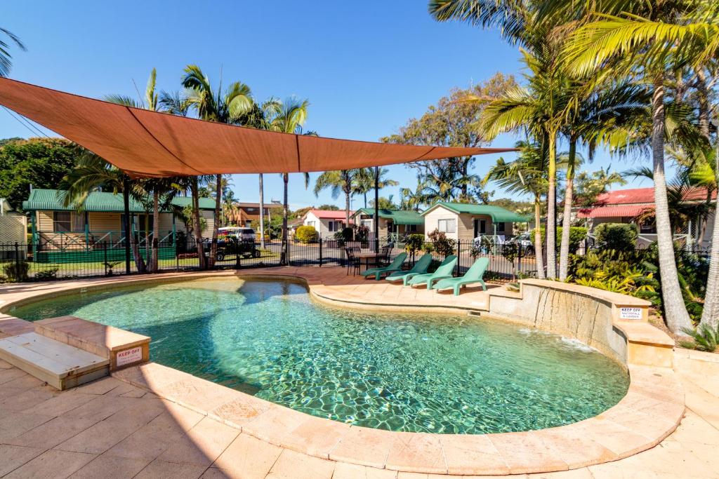 - une piscine avec des chaises et un grand parasol dans l'établissement Jacaranda Holiday Park, à North Haven