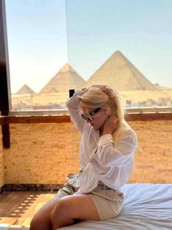 a woman sitting on a bed looking at the pyramids at Vida Pyramids Inn in Cairo