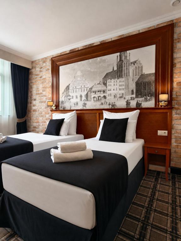two beds in a hotel room with a painting on the wall at Hotel Grodzki Business & Spa in Stargard