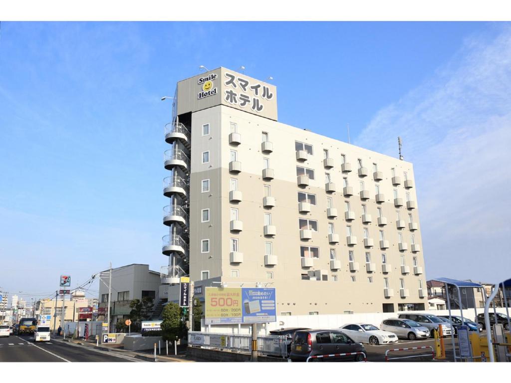un edificio blanco alto con coches estacionados en un estacionamiento en Smile Hotel Shiogama, en Shiogama