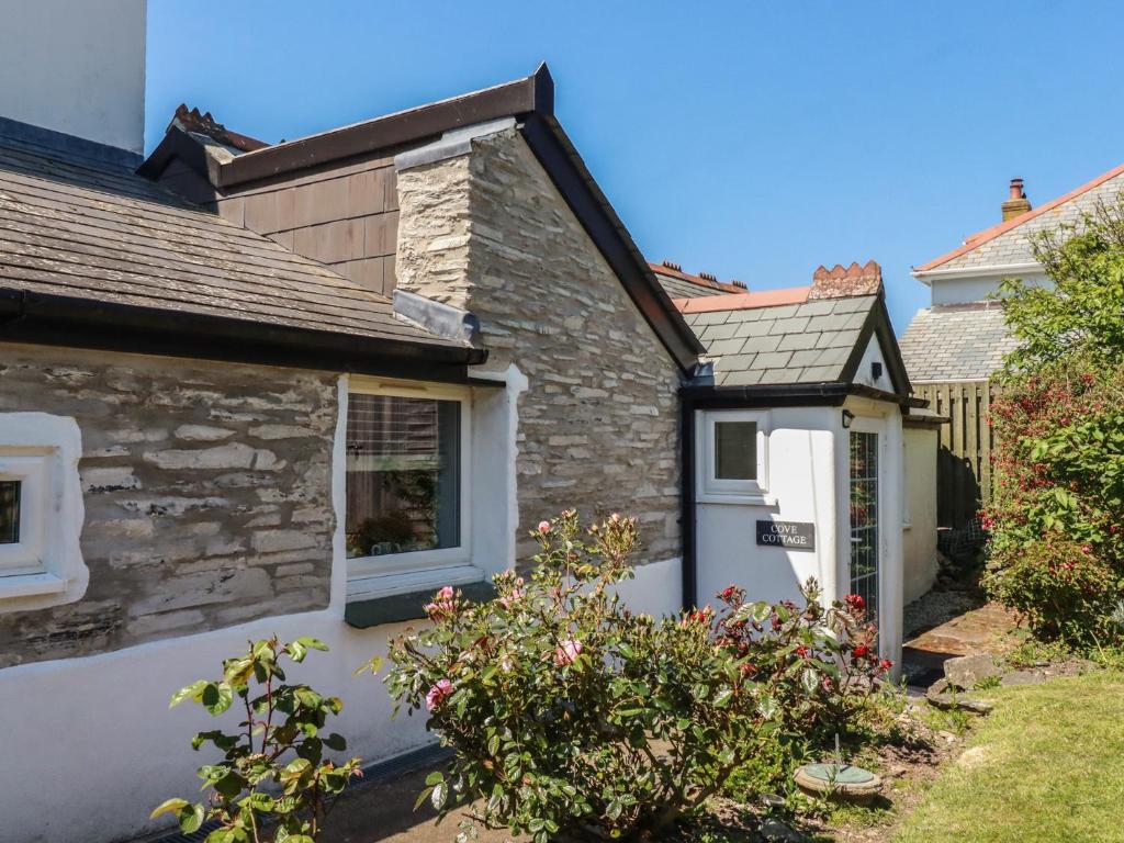 a stone cottage with a white door and a window at Cove Cottage in Tintagel