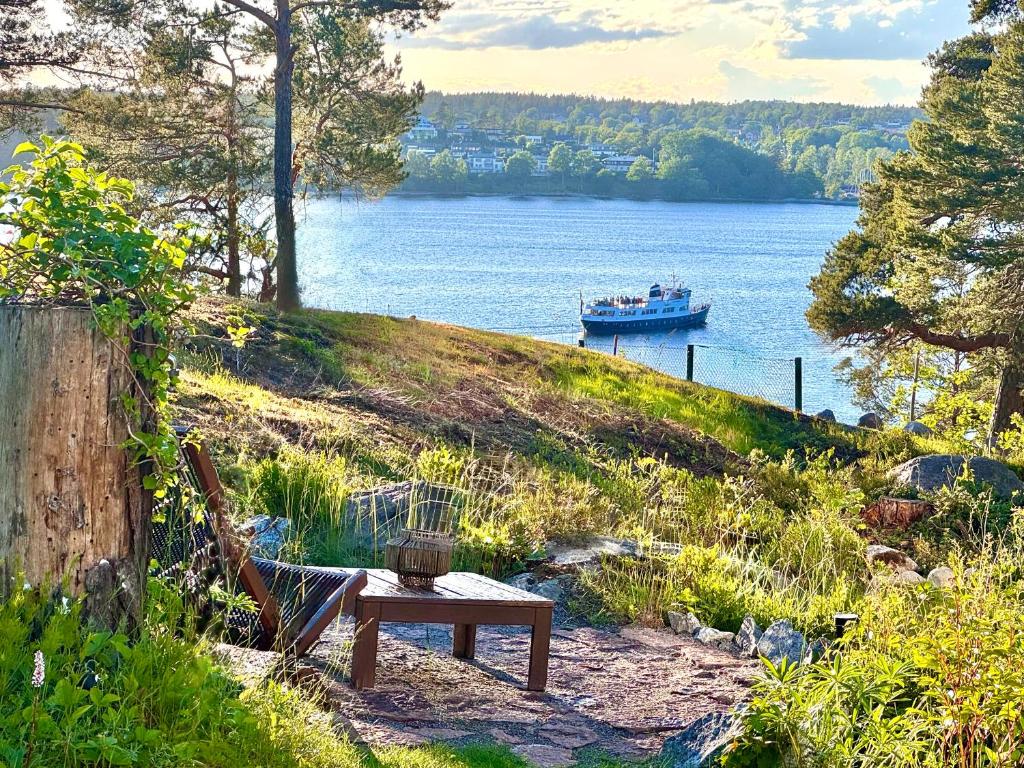 a bench on a hill with a boat in the water at Modern Seaside Guesthouse with Archipelago Views in Nacka