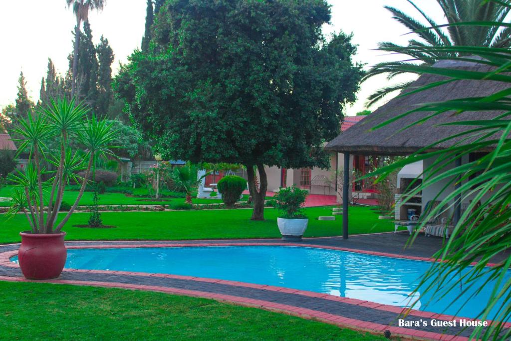 a swimming pool in a yard with trees and a house at Bara Guesthouse in Welkom