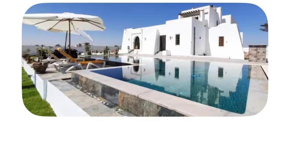 a white house with a swimming pool and an umbrella at Dar amiratt in El Guecheïne